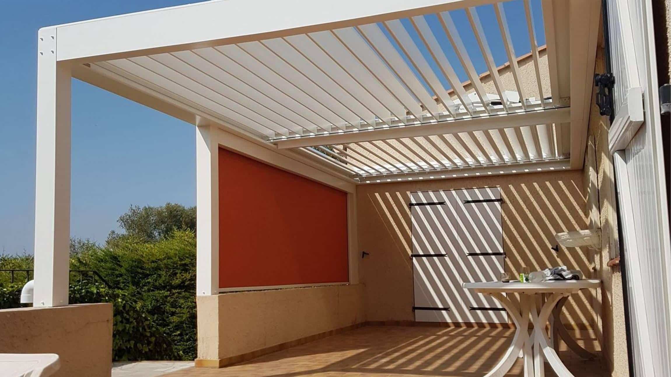 Pergola bioclimatique blanche à lames orientables avec store latéral orange sur une terrasse ensoleillée.